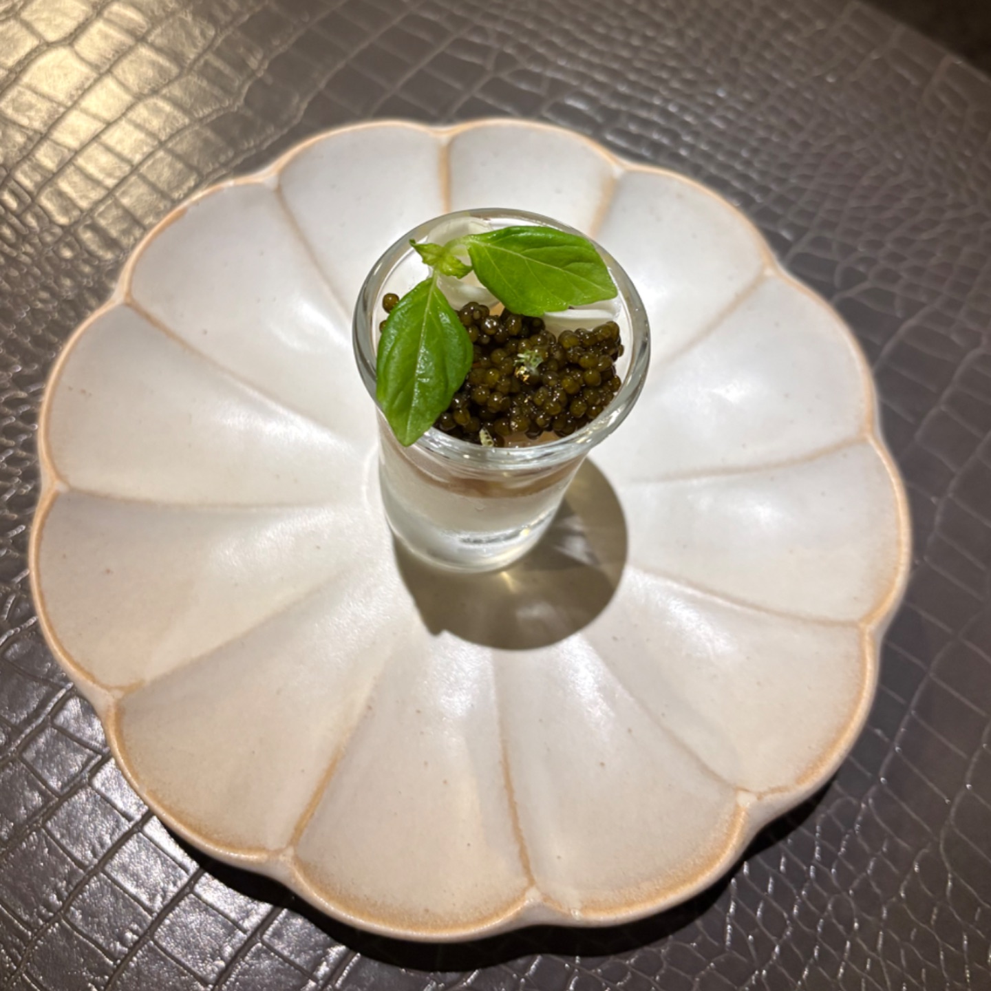 白い花形の皿に盛り付けたキャビアの前菜、バジルを添えて